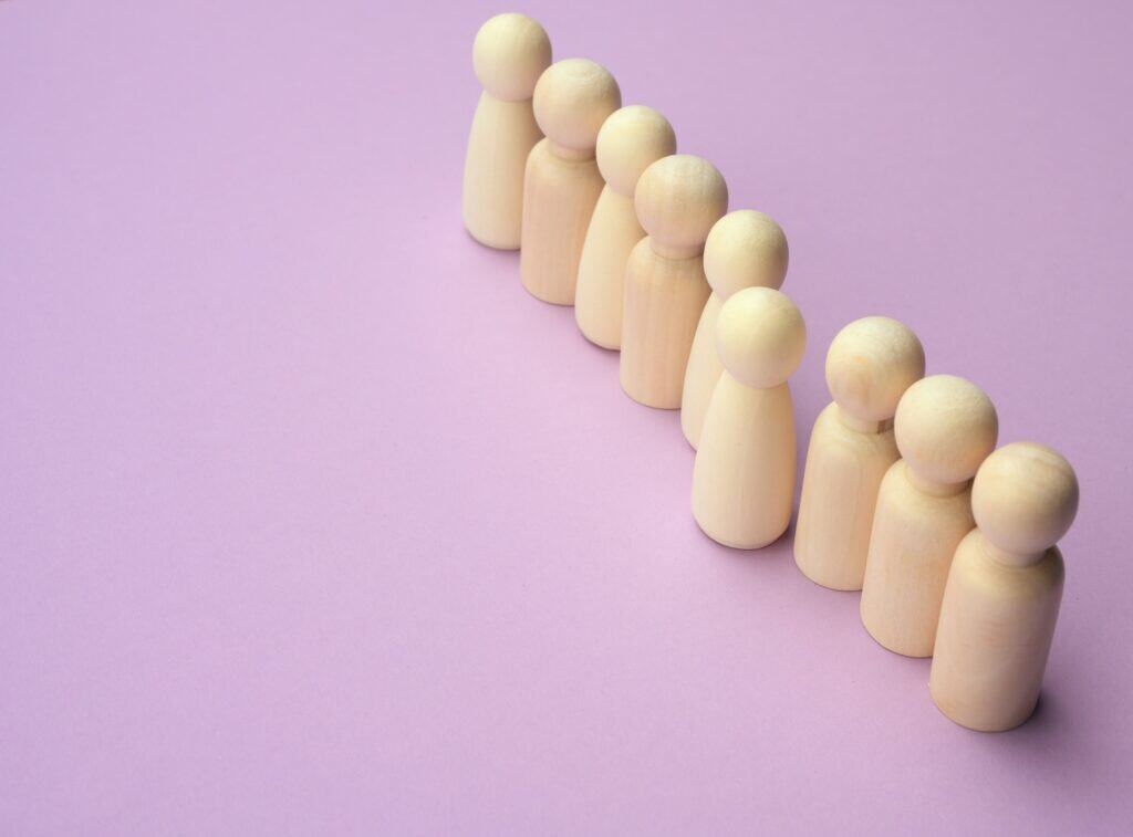 Wooden men stand in a row, one figurine sticking out in front.